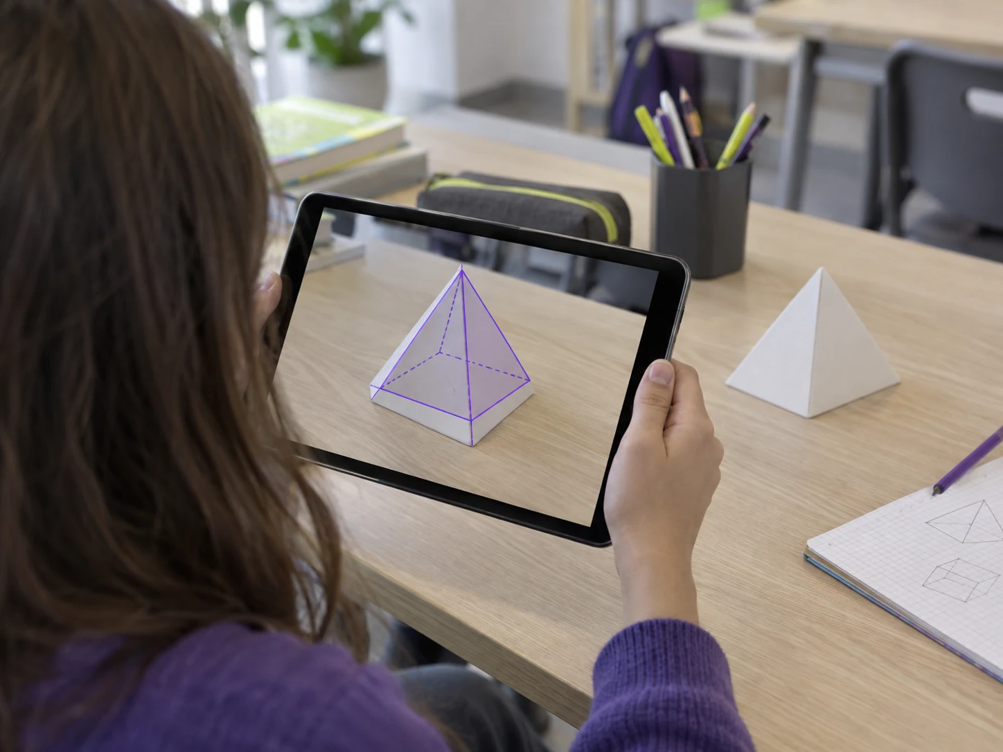 Estudiante utilizando una tablet con realidad aumentada, sin rostro visible.